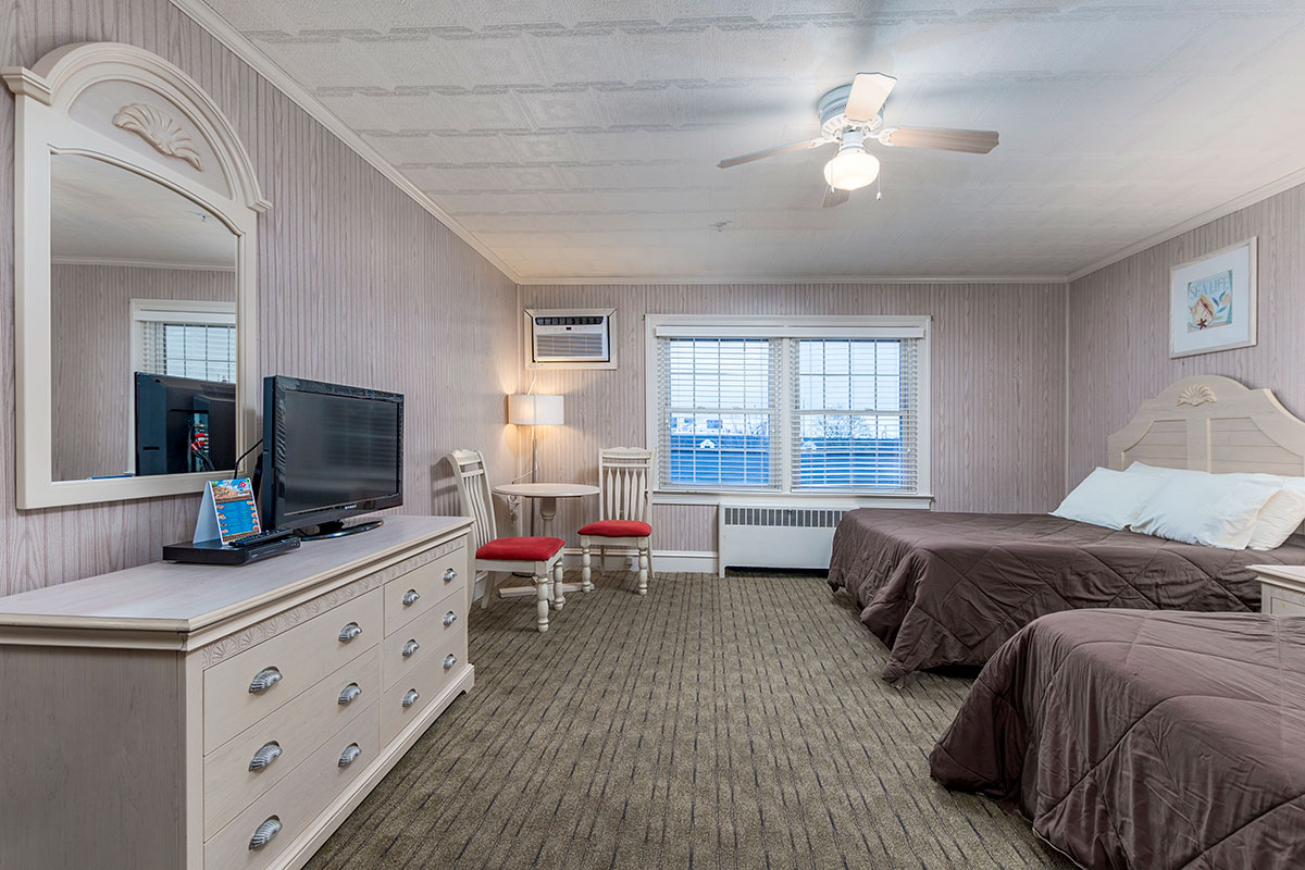 The Lodge room with flat screen tv on dresser, table with chairs, ceiling fan, and two beds